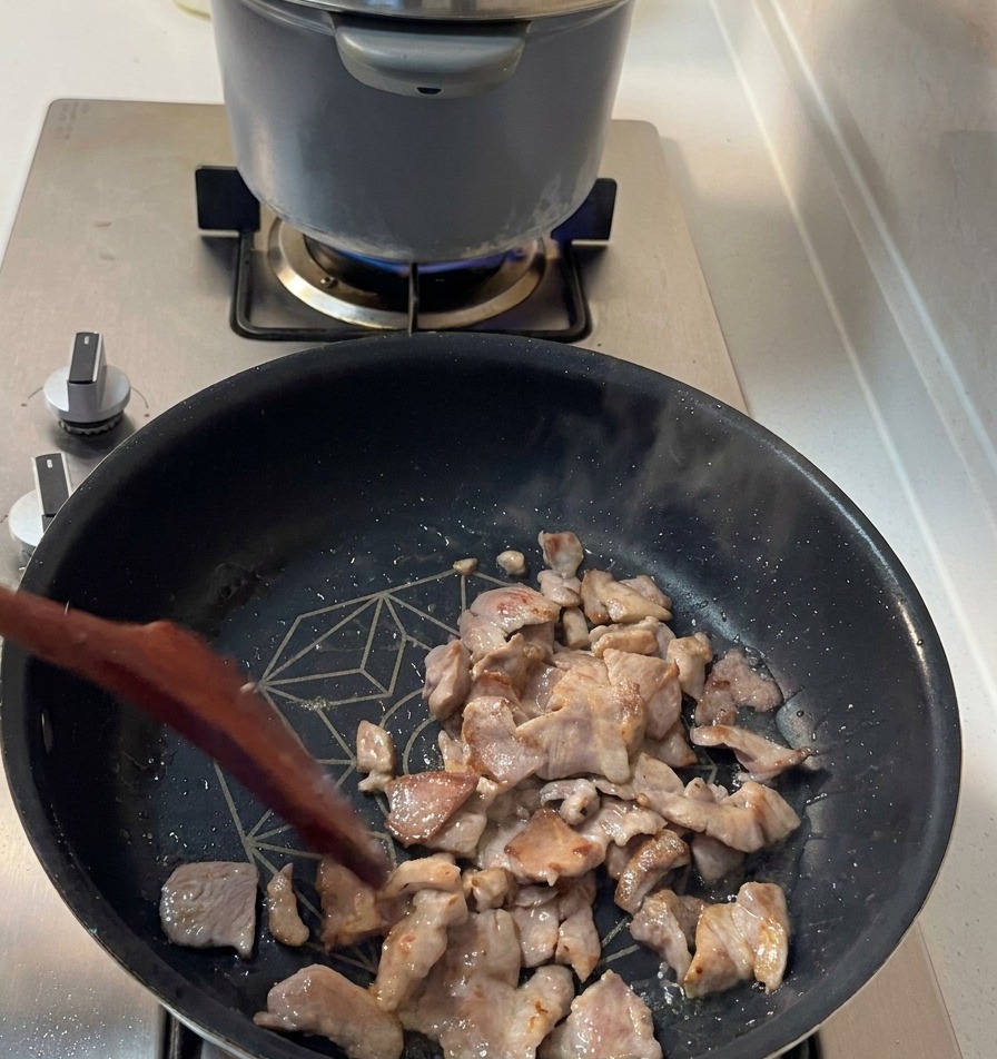 Bratende Schweinefleischstücke mit goldbraunen Rändern werden in einer dunklen Pfanne umgerührt.