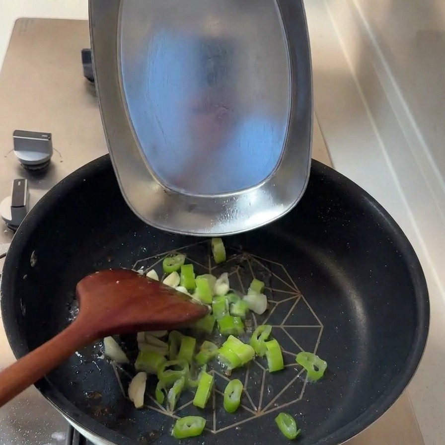 Gehackte Frühlingszwiebeln und Knoblauchscheiben werden in die Pfanne mit dem verbliebenen Bratfett gegeben.