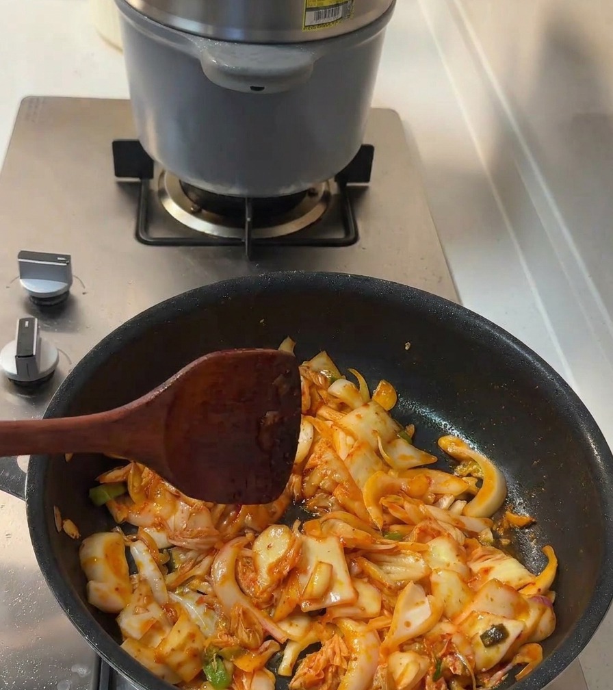 Flüssige Würze und weißer Zucker werden unter das bratende Kimchi und die Zwiebeln gemischt.