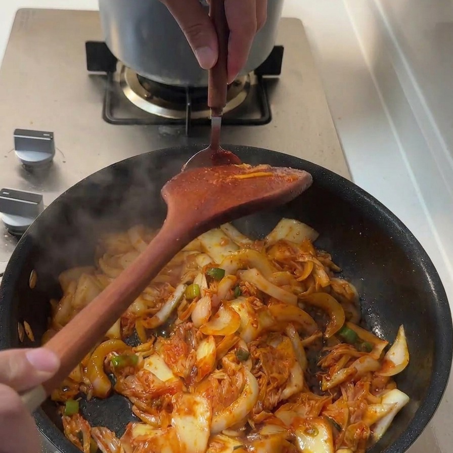 Ein Löffel dicke rote Gochujang-Paste wird in die Pfanne zu den restlichen Zutaten gegeben.