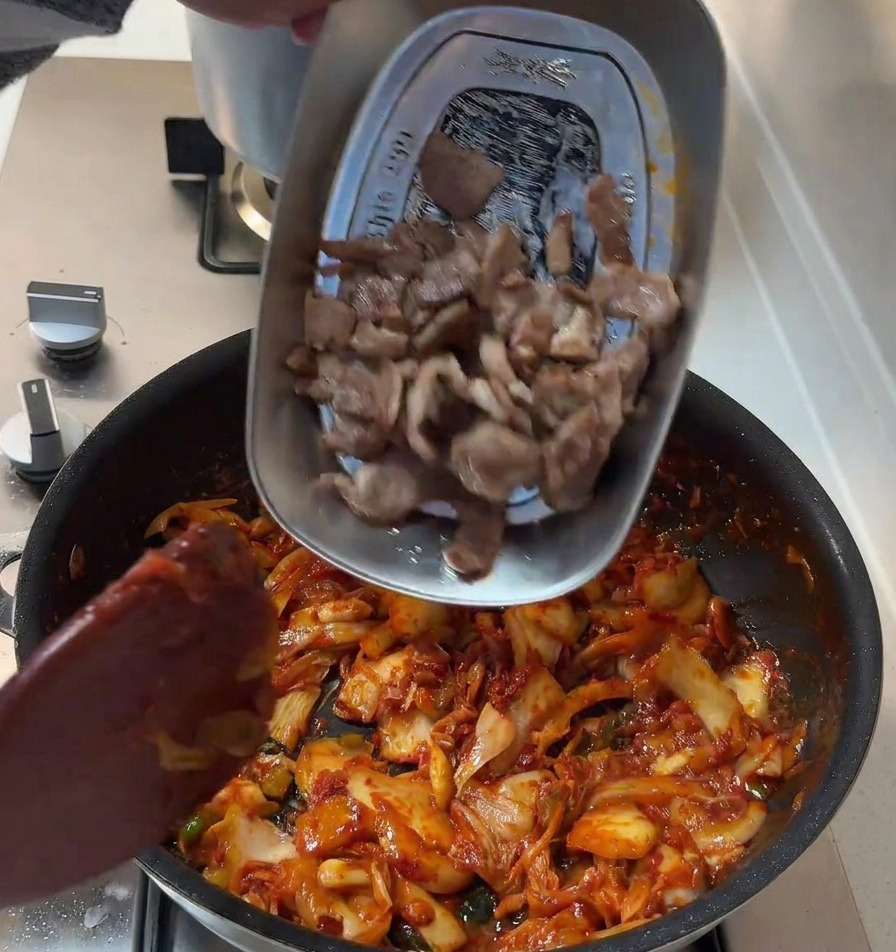 Die angebratenen Schweinefleischscheiben werden zurück in die Pfanne zur roten Kimchi-Zwiebel-Mischung gegeben.
