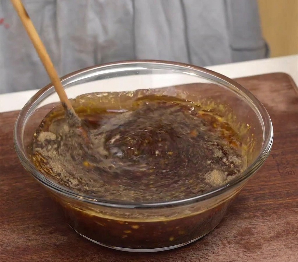 Ein Holzlöffel rührt eine dunkle, aromatische koreanische Marinade in einer klarsichtigen Glasschüssel um.