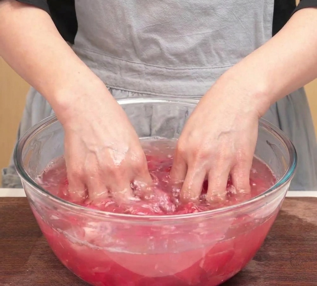 Hände drücken eine Portion gewaschenes rohes Rindfleisch über einer Schüssel aus, um überschüssiges Wasser zu entfernen.