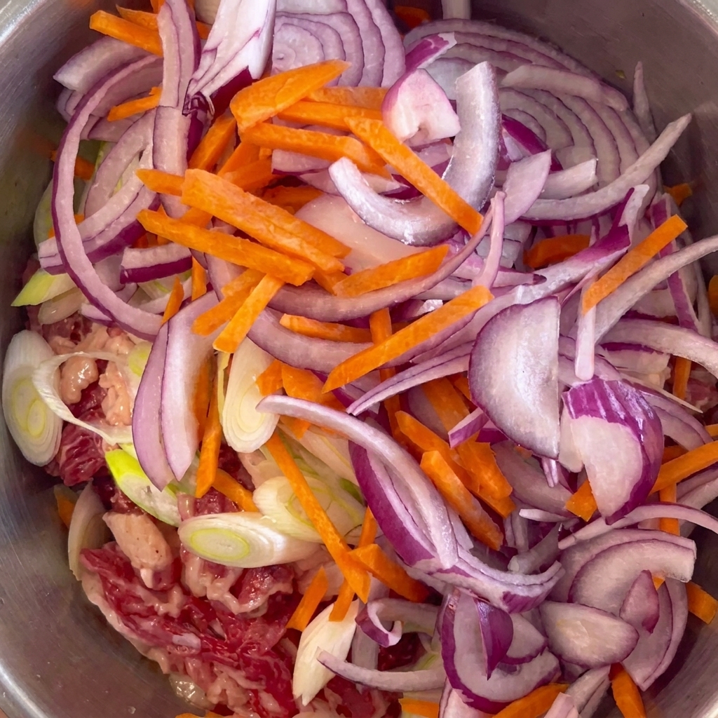 Rote Zwiebeln und leuchtend orangefarbene Karottenstreifen liegen auf dem marinierten Rindfleisch.