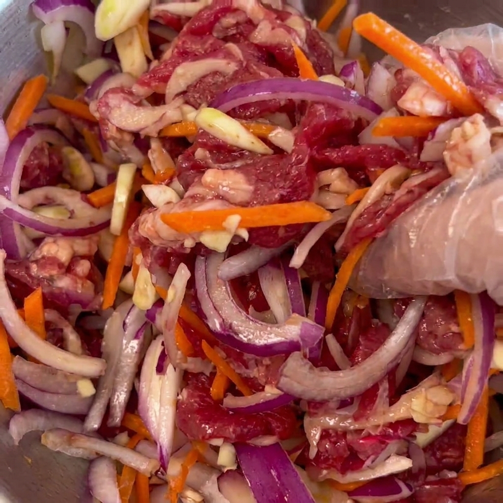 Zutaten wie Rindfleisch, Zwiebeln und Karotten werden in einer Metallschüssel mit der Hand vermischt.