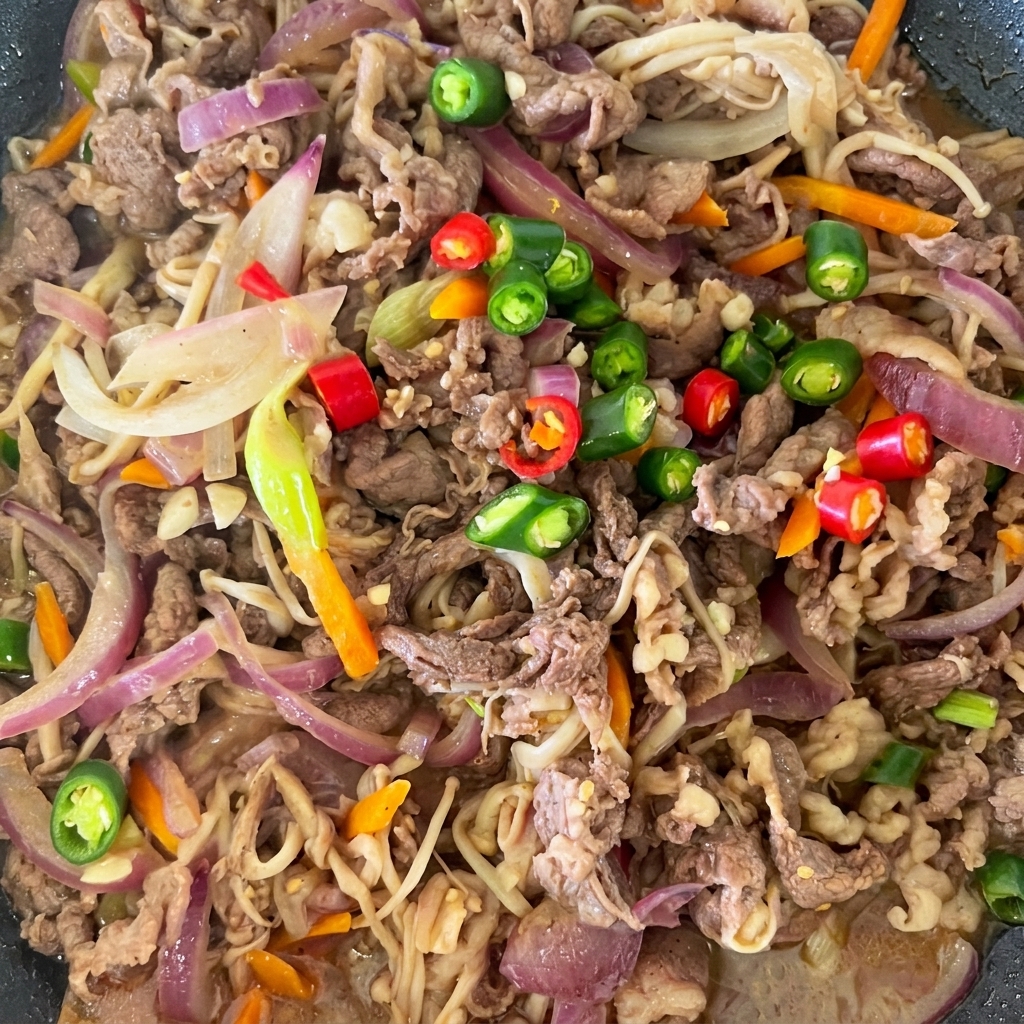 Rote und grüne Chilischeiben als Topping auf dem fertigen Bulgogi in der Pfanne.
