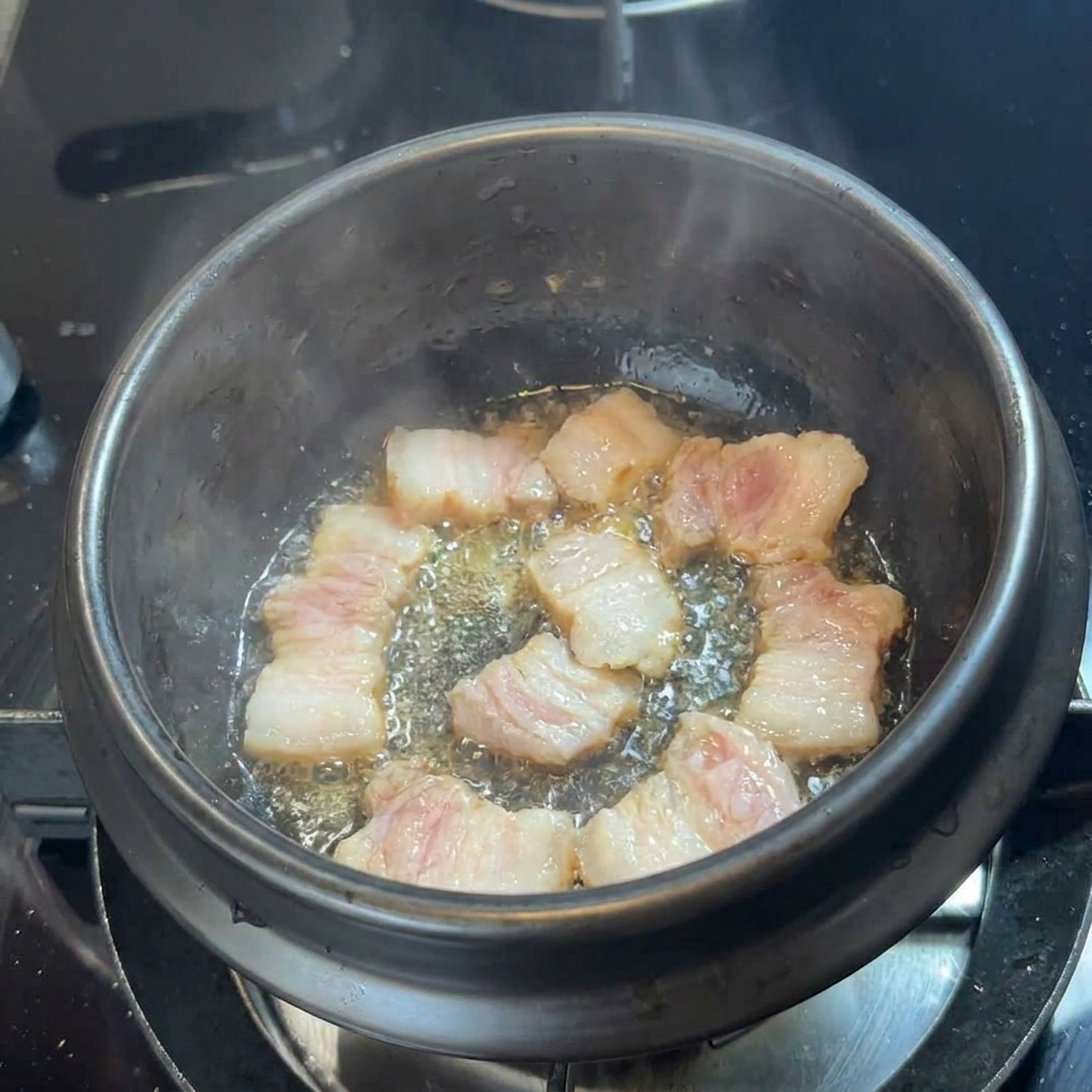 In einem schwarzen Steintopf brutzelt Schweinebauch im eigenen Fett.