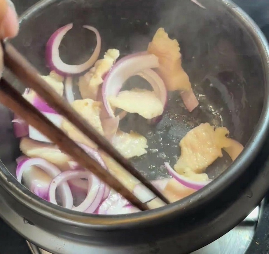Frische rote Zwiebelspalten werden mit dem Schweinebauch im Topf vermengt.