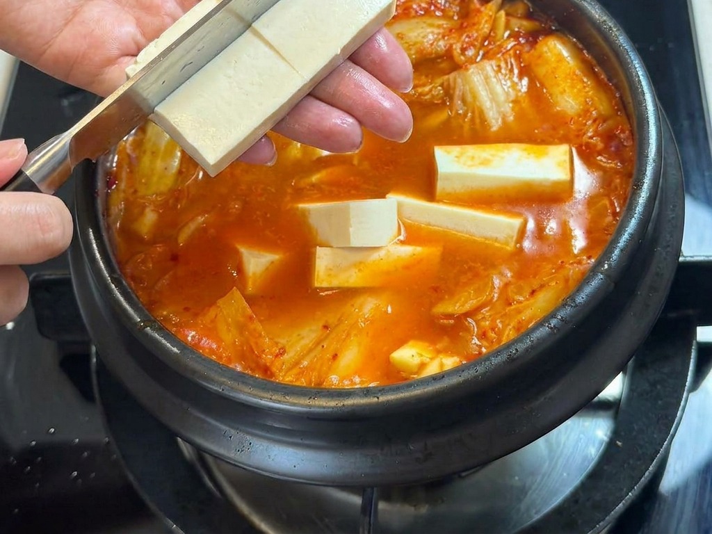 Tofu wird mit einem Messer direkt über dem kochenden Eintopf in Würfel geschnitten.