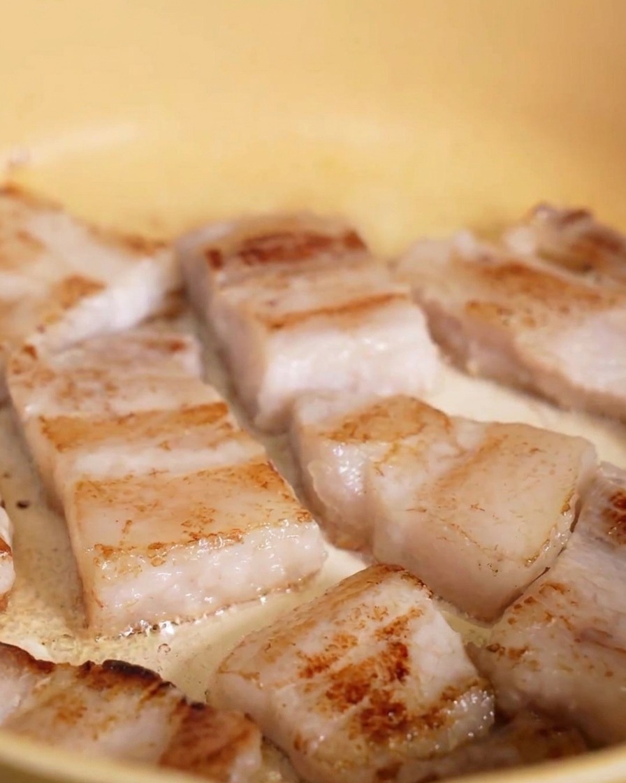 Schweinebauchscheiben in einer gelben Pfanne, deren Unterseiten eine deutliche goldbraune Kruste zeigen.