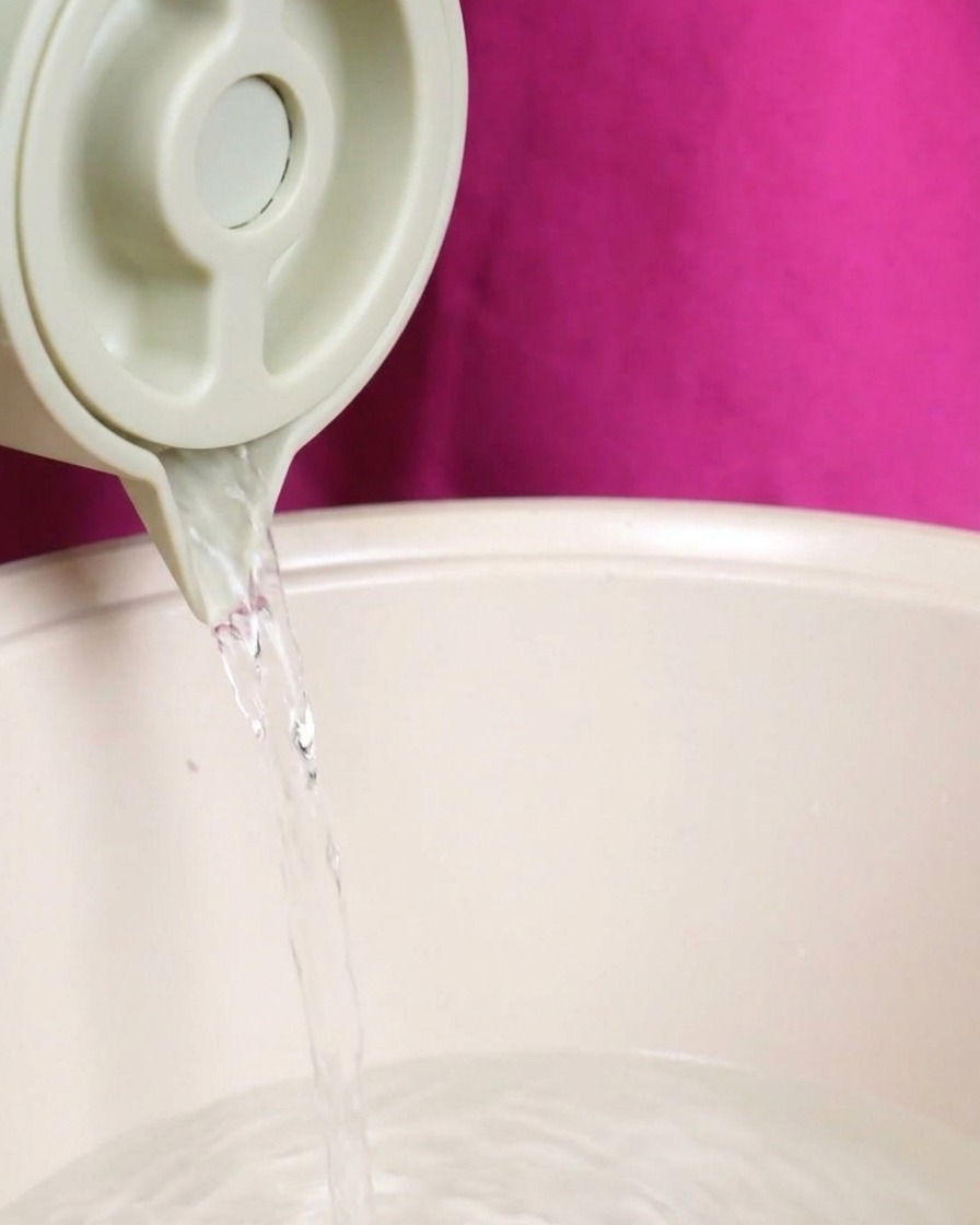 Ein Strahl klares Wasser wird aus einem Krug in den Topf mit den Suppenzutaten gegossen.