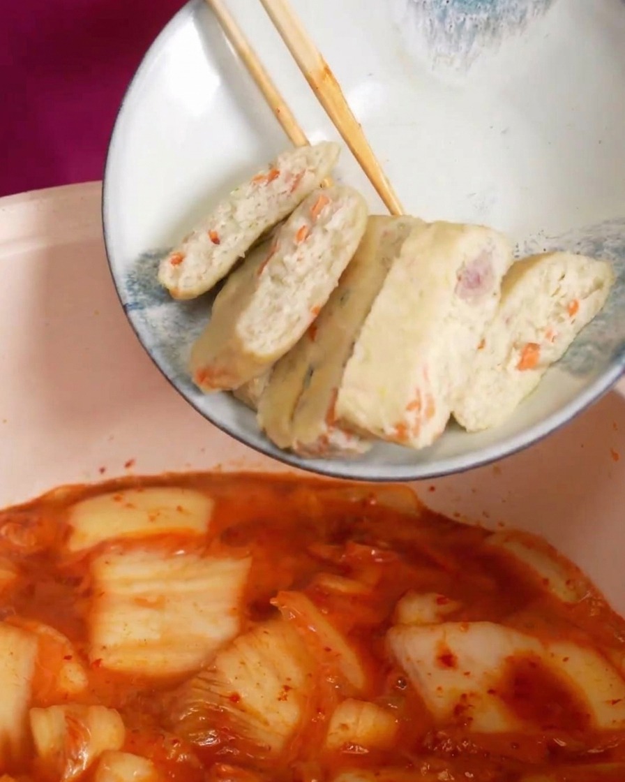 Helle Fischkuchen-Scheiben mit Gemüsestückchen werden in die kochende rote Suppe gegeben.