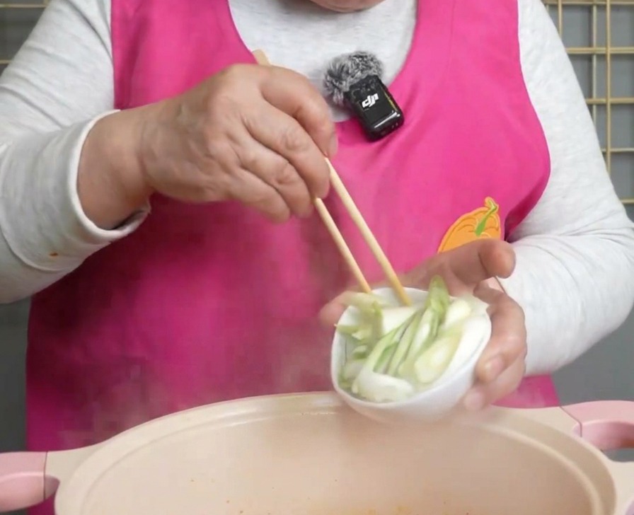 Frisch gehackte Frühlingszwiebeln werden aus einer Schale in die dampfende Suppe gestreut.
