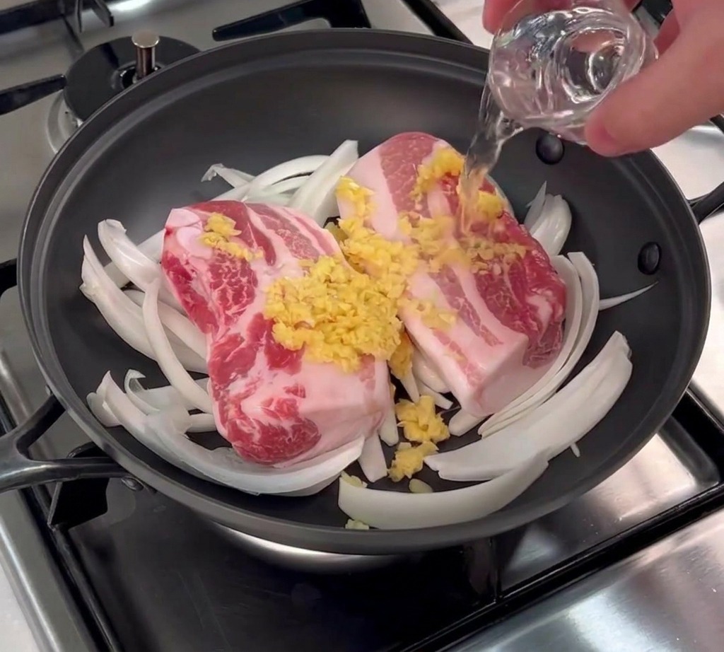 Reiswein wird aus einem kleinen Glas über den Schweinebauch und den Knoblauch gegossen.