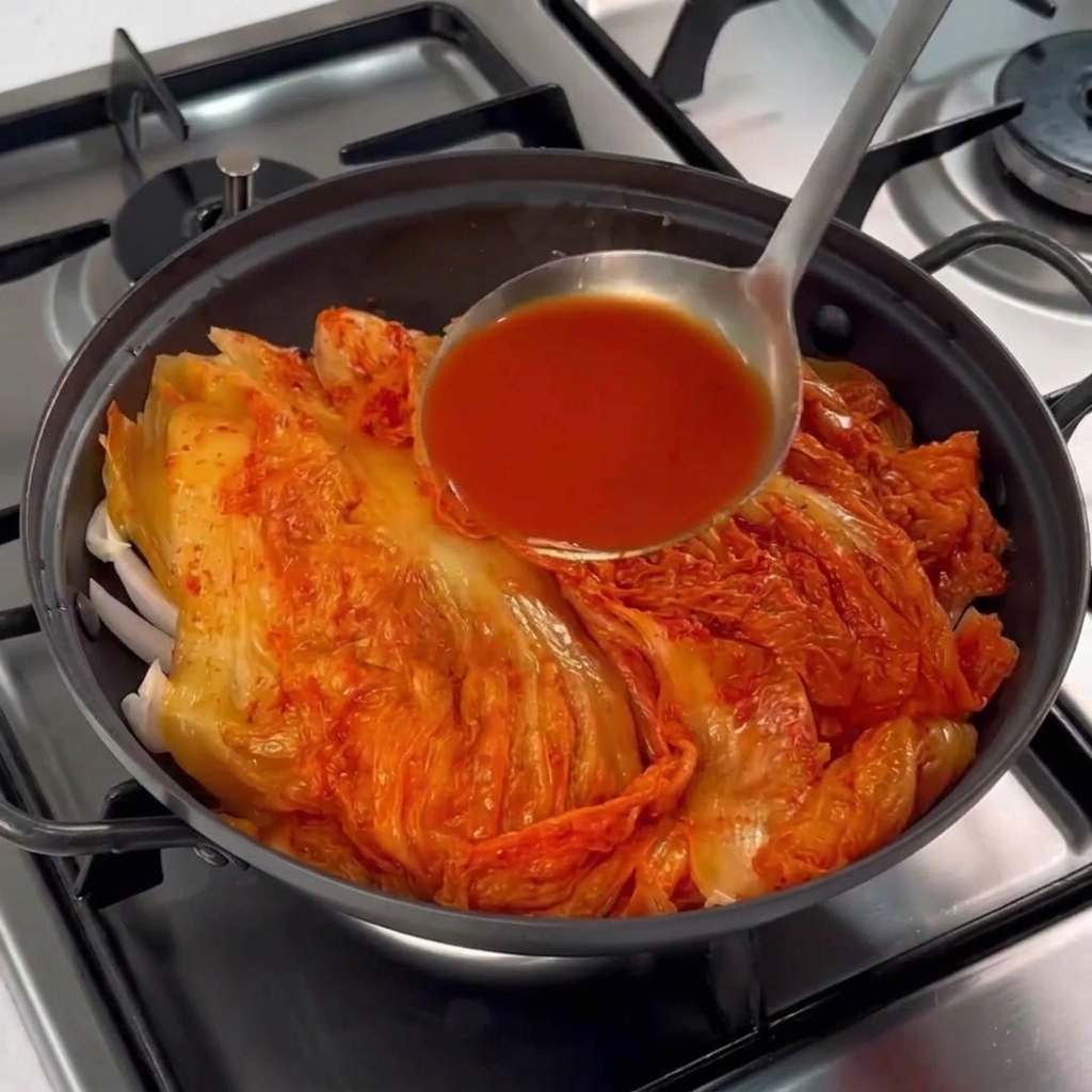 Rote Kimchi-Lake wird mit einer Kelle über den Kimchi und das Fleisch im Topf gegossen.