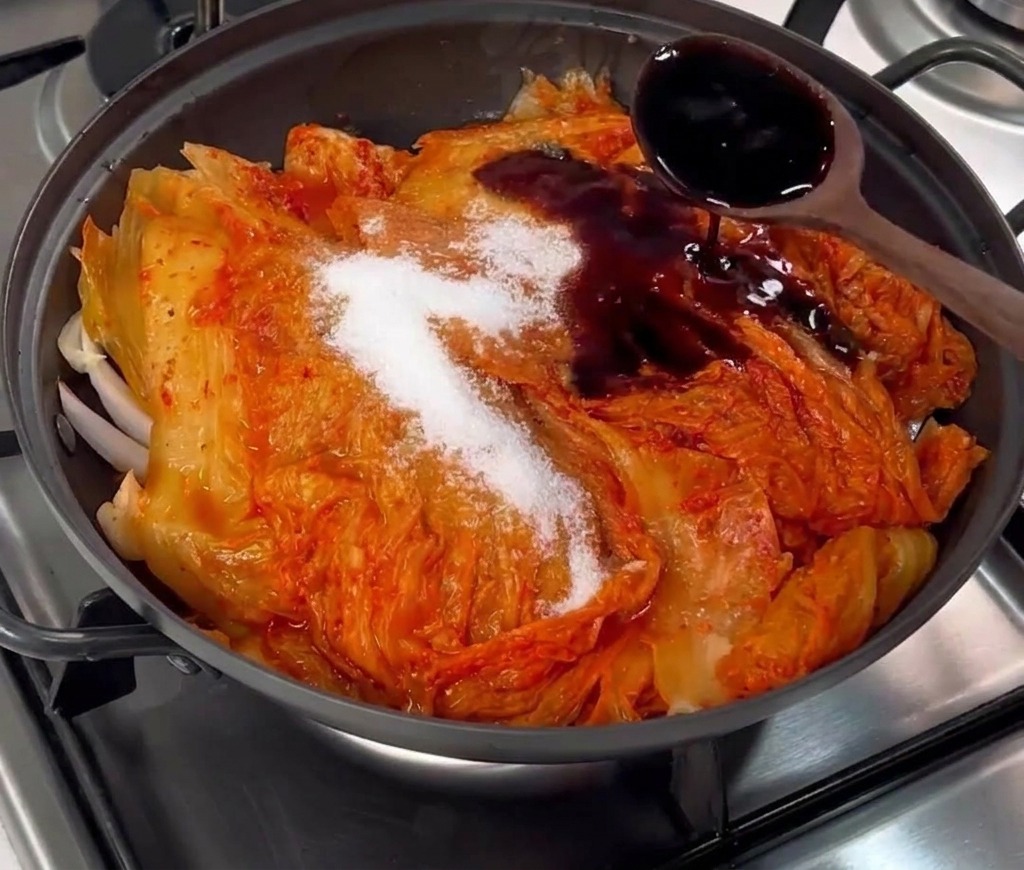 Dunkle Sojasauce wird über den Kimchi und den Zucker in die Pfanne gegossen.