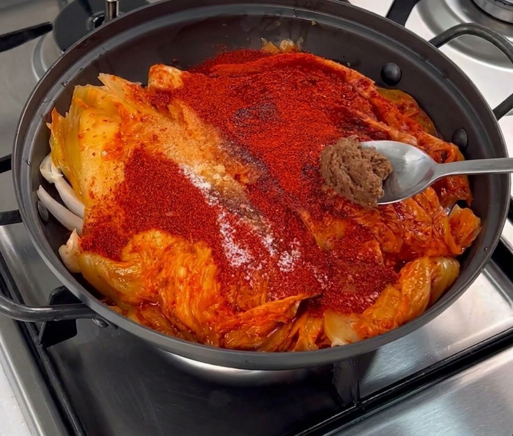 Ein kleiner Klecks braune Sojabohnenpaste auf einem Metalllöffel über dem Kimchi.