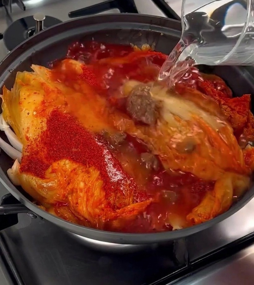 Klares Wasser wird aus einem Krug in den Topf mit Kimchi und Schweinebauch gegossen.