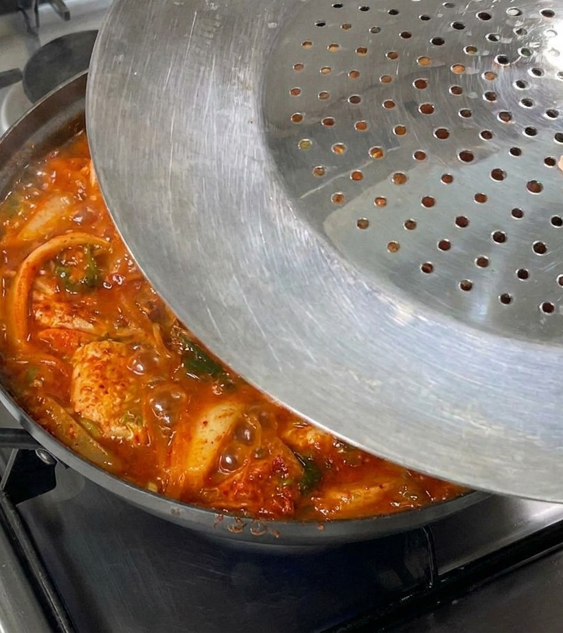 Ein Metalldeckel wird auf den dampfenden Topf mit Kimchi-Eintopf gesetzt.