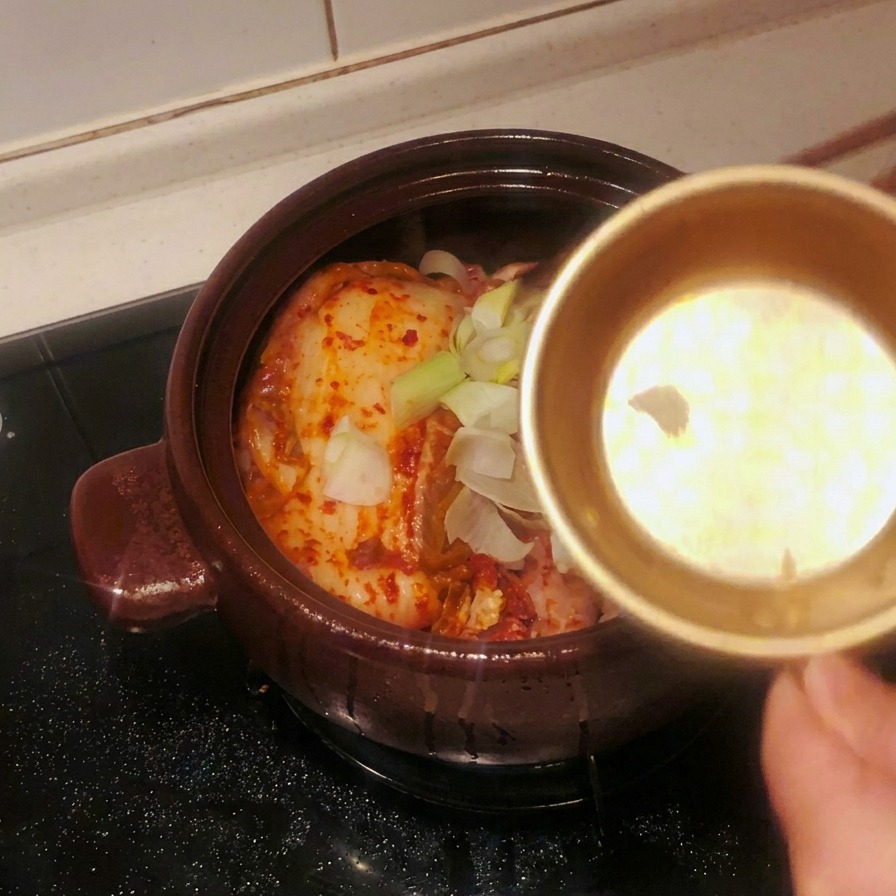 Geschnittener Knoblauch und grobe Frühlingszwiebelstücke werden aus einer Schale auf den Kimchi im Topf gestreut.