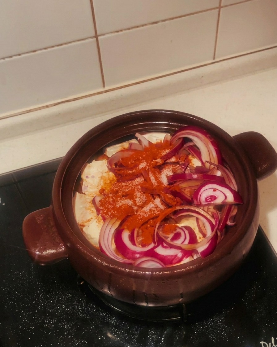 Weißer Zucker wird über die Zutaten und das Chilipulver im Tontopf gestreut.