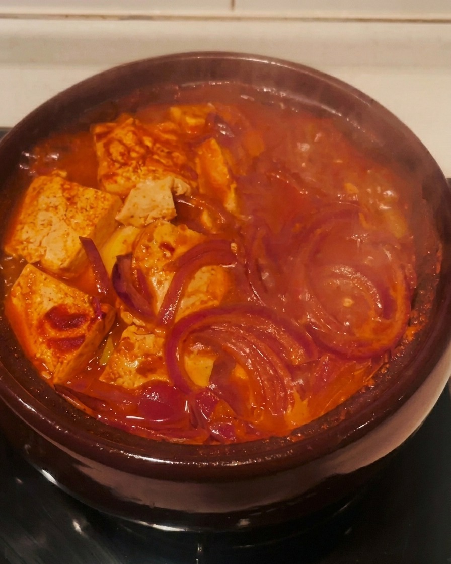 Der fertig gekochte Kimchi-Eintopf sprudelt kräftig rot im Tontopf auf dem Herd.