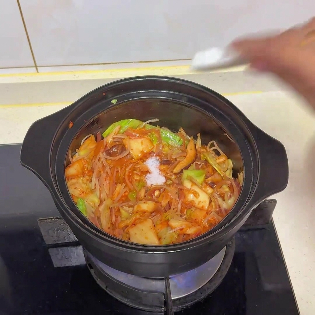 Eine Prise weißes Salz wird in den Topf mit dem gebratenen Gemüse und Kimchi gestreut.