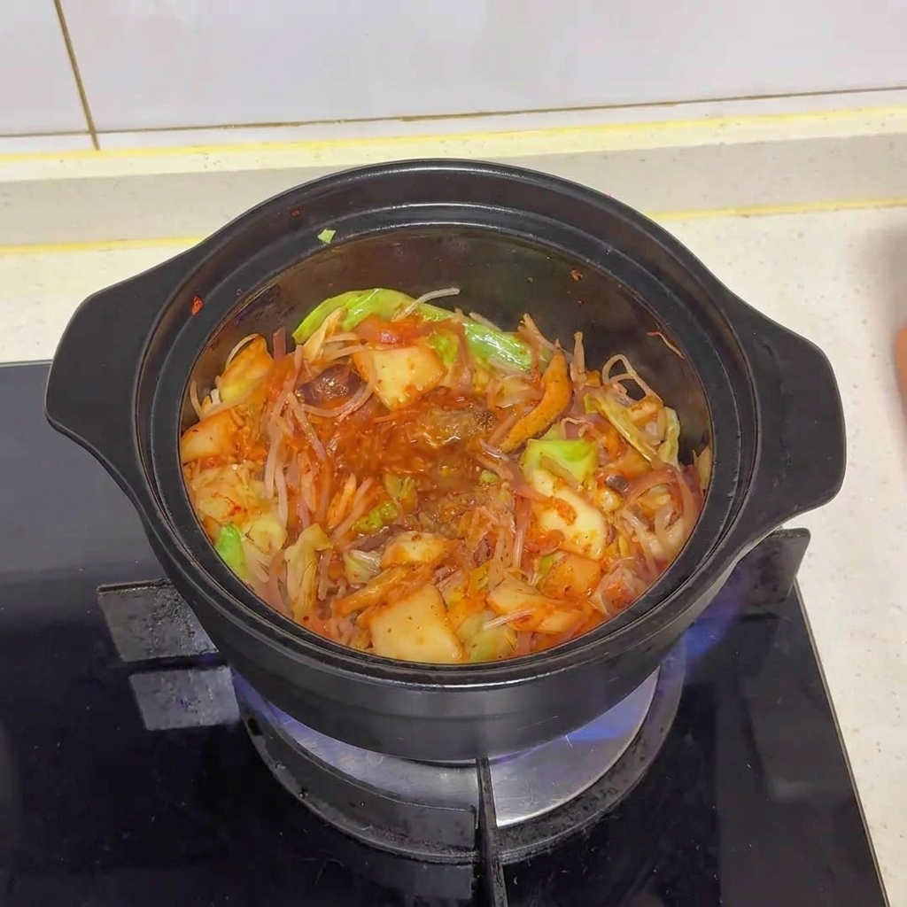 Die Gemüse-Kimchi-Mischung im Topf nach der Zugabe von Brühepulver und MSG, wobei sich die Gewürze gerade vermischen.