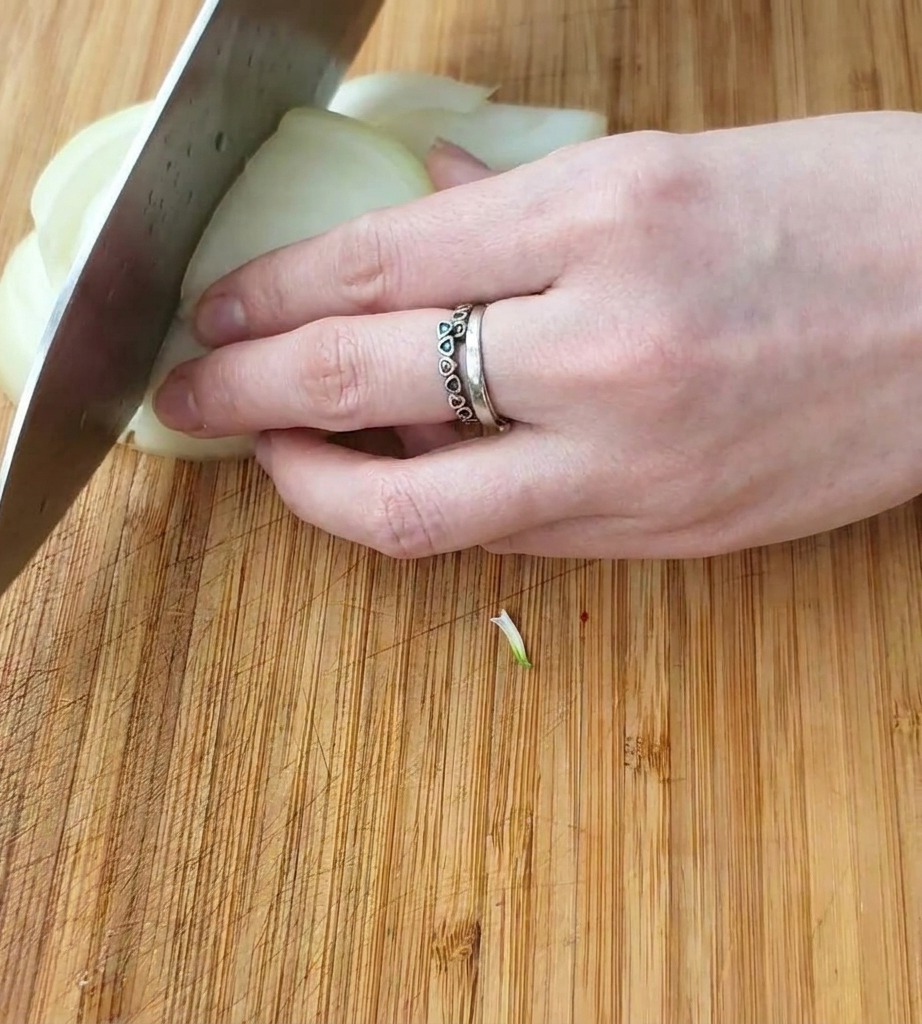 Nahaufnahme einer Hand, die eine weiße Zwiebel mit einem Kochmesser auf einem Holzbrett in gleichmäßige Würfel schneidet.
