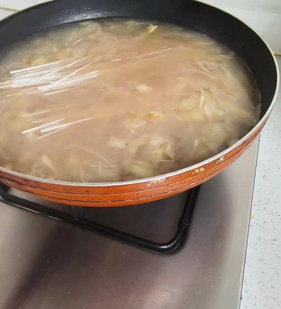 Eine Handvoll trockene, durchsichtige Glasnudeln wird in die köchelnde Sojabohnenpaste-Suppe gegeben.