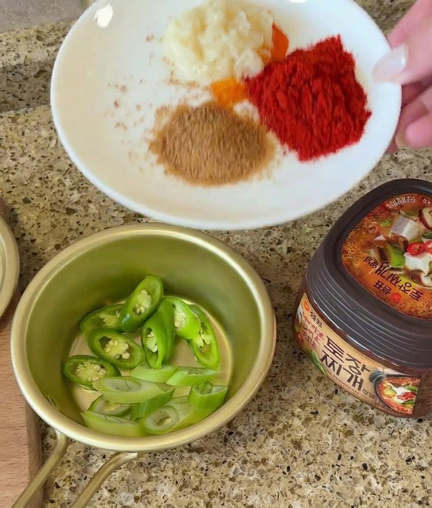 Knoblauch, Gewürze und eine Schale mit geschnittenen Chilis stehen bereit neben einem Glas Sojabohnenpaste.