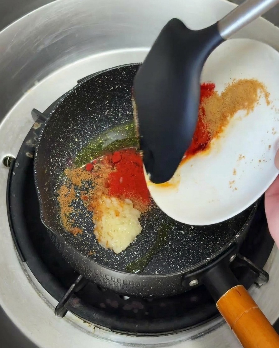 Knoblauch und Chilipulver werden in einer Pfanne mit Öl unter Rühren angebraten.