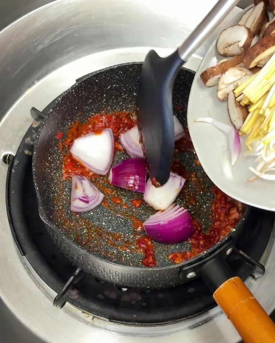 Rote Zwiebeln und Pilze werden in der Pfanne mit der roten Gewürzbasis vermengt.