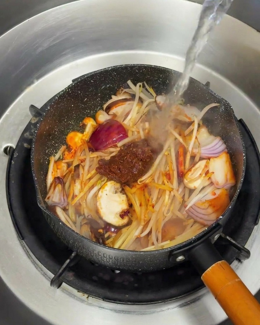 Heißes Wasser wird über das angebratene Gemüse und die Sojabohnenpaste gegossen.