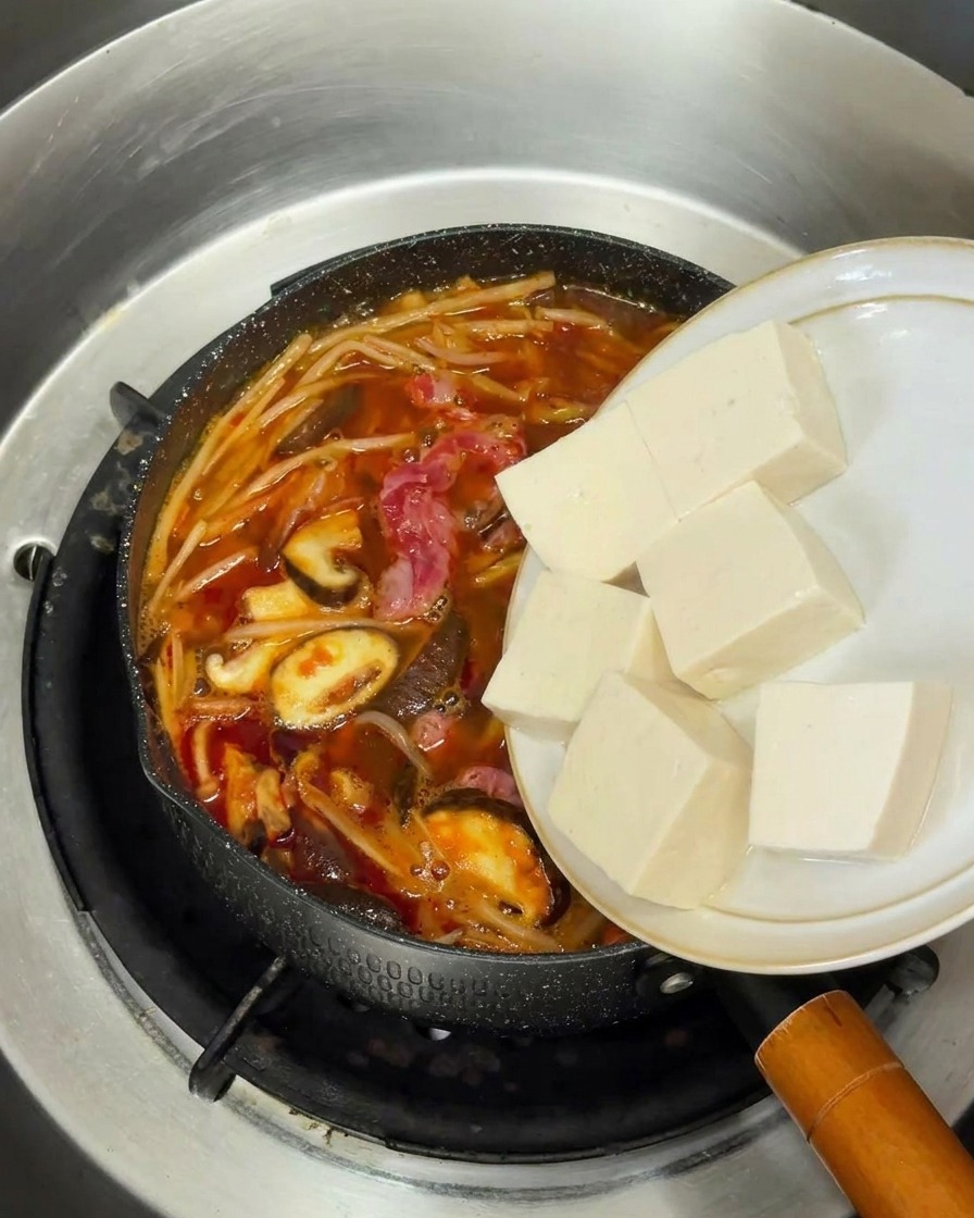 Frische Würfel aus weißem Seidentofu werden in den Topf mit der kochenden Suppe gleiten gelassen.