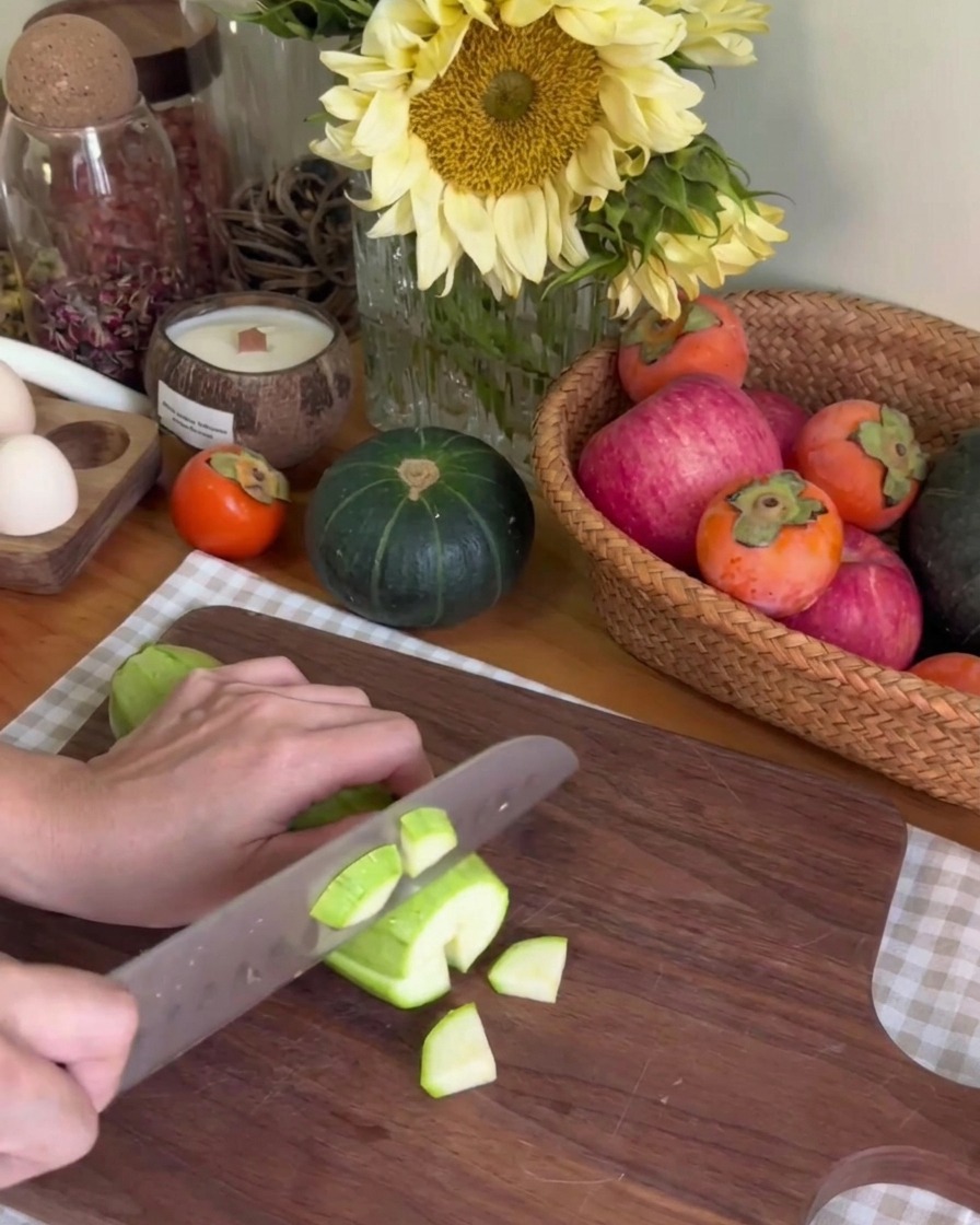 Eine Person schneidet eine grüne Zucchini auf einem dunklen Holzschneidebrett in kleine Stücke