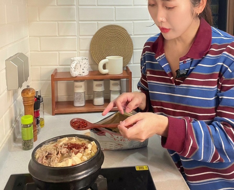 Ein Holzlöffel gibt leuchtend rotes Chilipulver in den Eintopf mit Fleisch, Tofu und Zucchini
