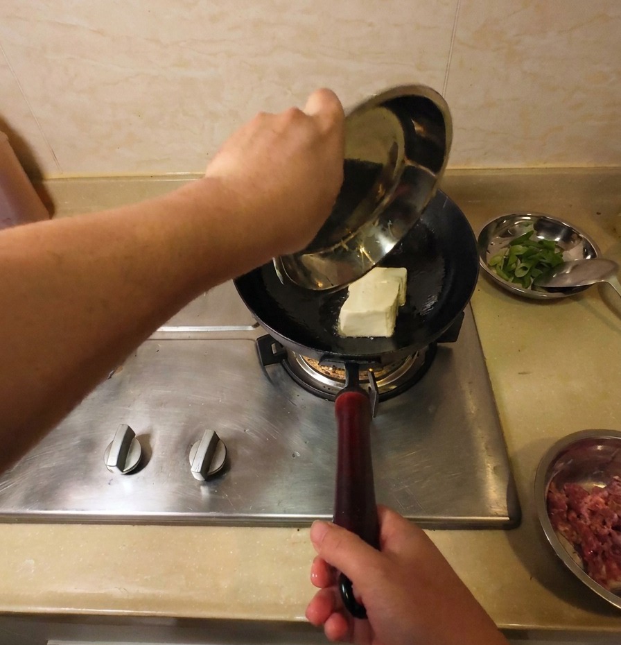 Ein ganzer Block weißer Tofu wird vorsichtig in den heißen Wok mit schimmerndem Öl gegeben.