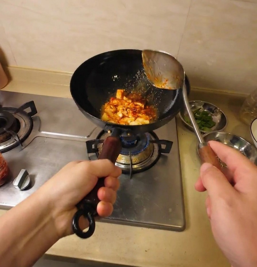 Die Tofustücke werden im schwarzen Wok gründlich mit der würzigen roten Sauce vermengt.