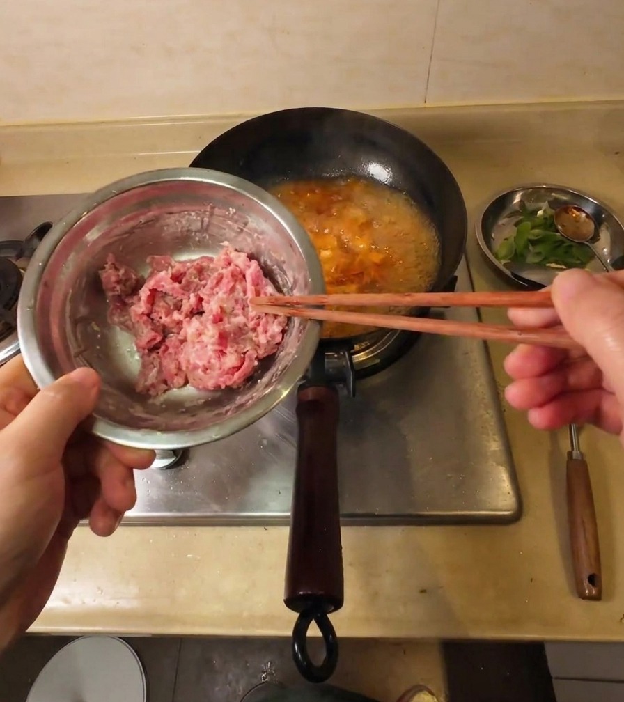 Dünne, mit Stärke bestäubte Rindfleischstreifen werden mit Stäbchen einzeln in die kochende Suppe gegeben.