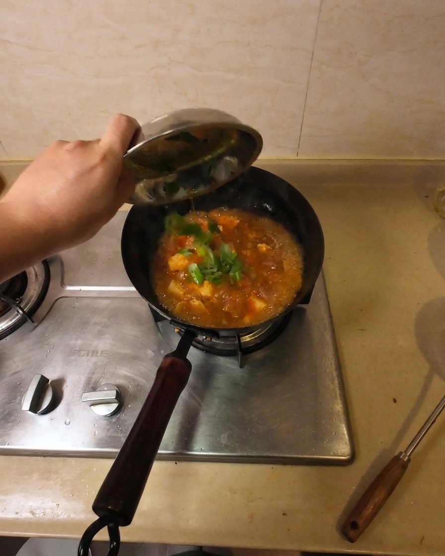 Frisch gehackte Frühlingszwiebeln werden aus einer kleinen Schale in die simmering Suppe gestreut.