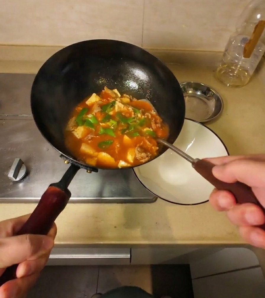 Die fertige, sämige Suppe wird aus dem geneigten Wok in eine weiße Servierschale umgefüllt.