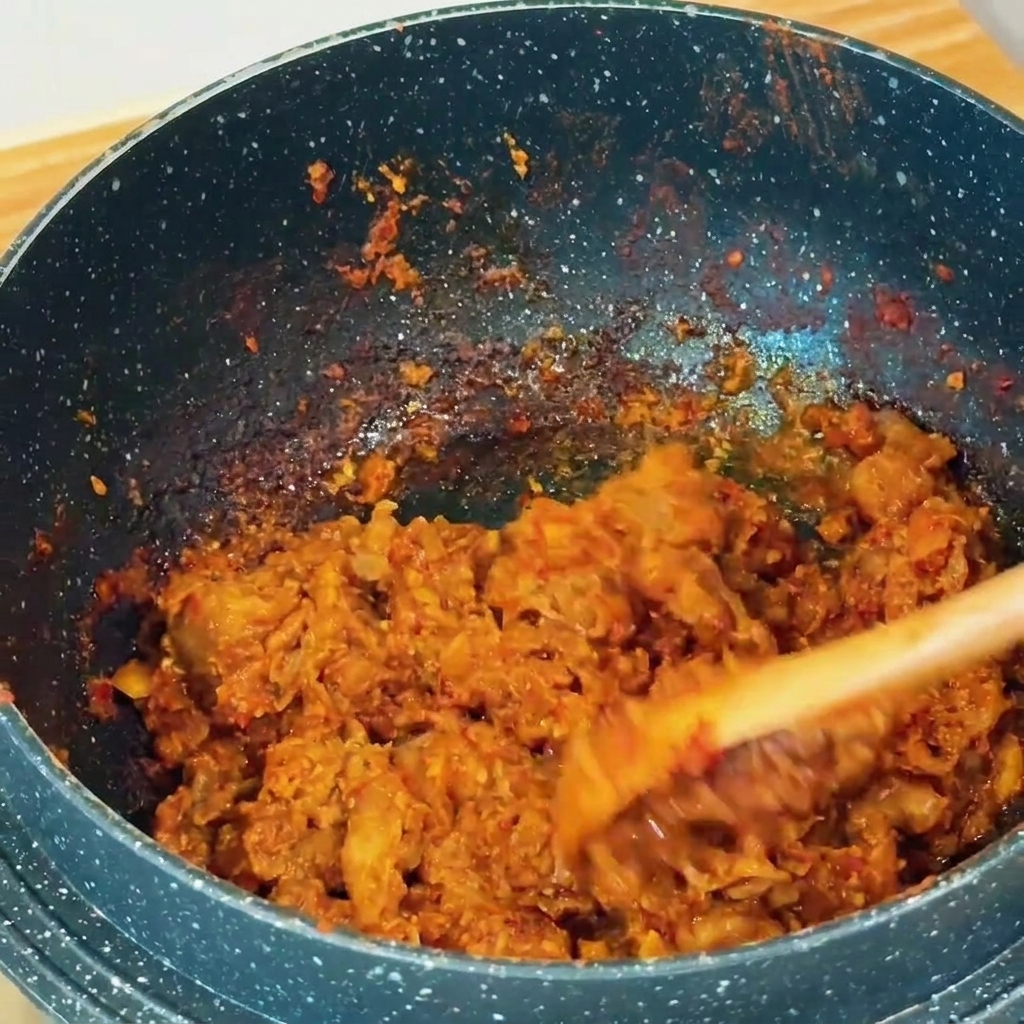 Dünne Rindfleischscheiben werden mit rötlich-brauner Sojabohnenpaste in einem dunklen Topf mit einem Holzspatel angebraten.