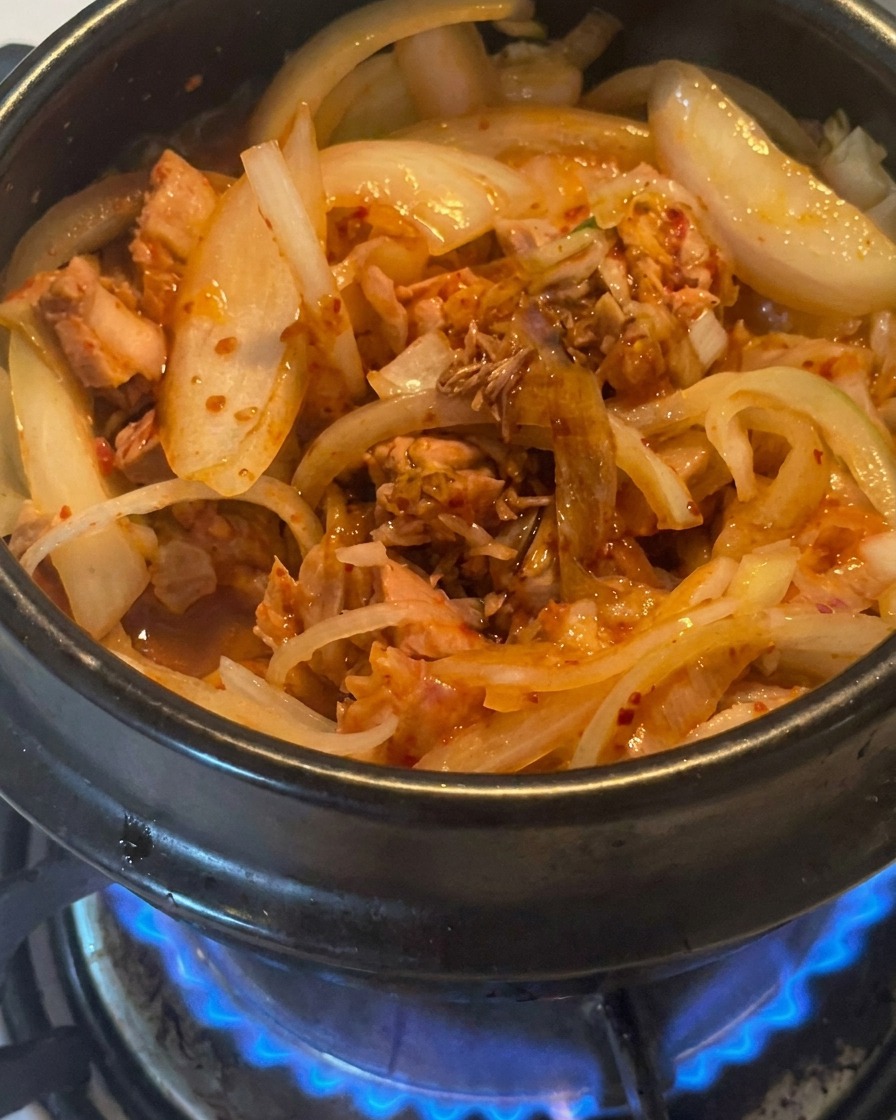 Dunkle Sojasauce wird über die Mischung aus Thunfisch und Kimchi im Topf geträufelt.