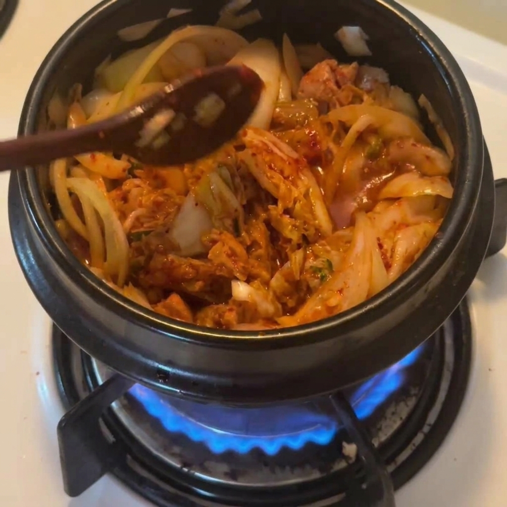 Ein Holzlöffel streut rotes koreanisches Chilipulver über den Thunfisch-Kimchi-Mix.