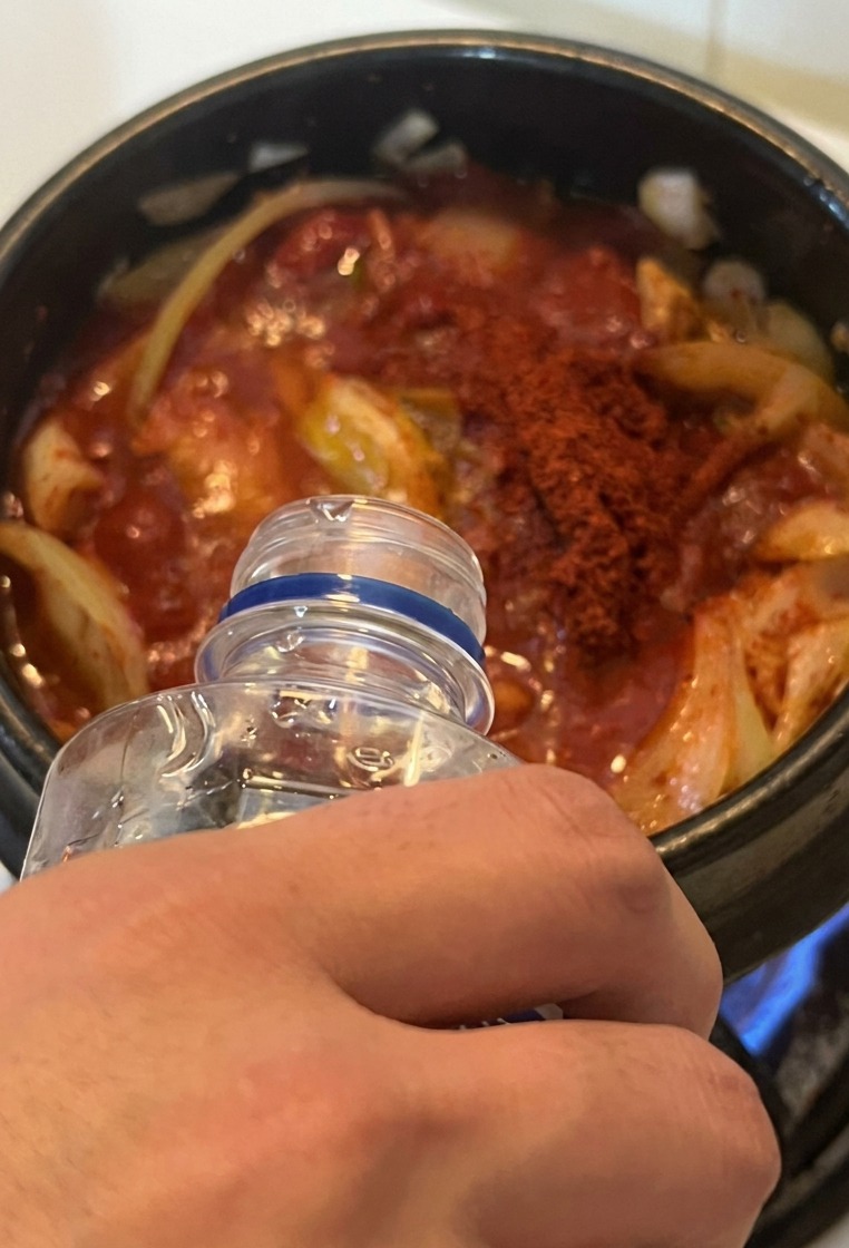 Wasser wird aus einer Flasche in den Topf mit dem roten Kimchi-Thunfisch-Eintopf gegossen.