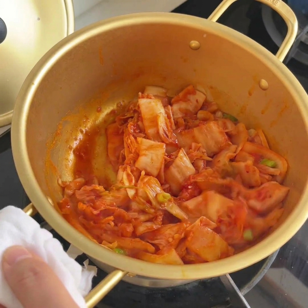 Gebratenes Kimchi und Frühlingszwiebeln werden in einem goldenen Topf vermischt, bis der Kohl glasig aussieht.