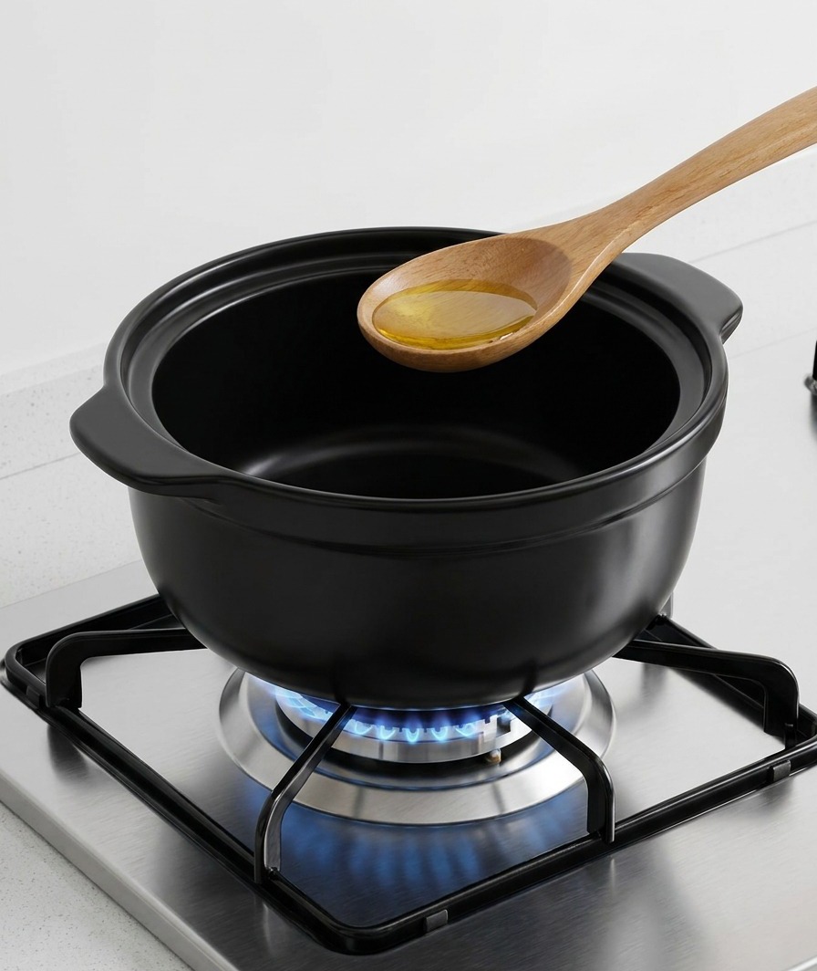 Ein Holzlöffel gießt goldenes Sesamöl in einen dunklen Keramiktopf über einer Gasflamme.