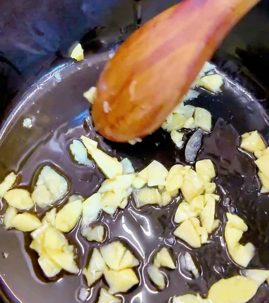 Gehackte Stücke von rotem, scharfem Kimchi werden mit einem Holzlöffel in den Topf mit Knoblauch gerührt.