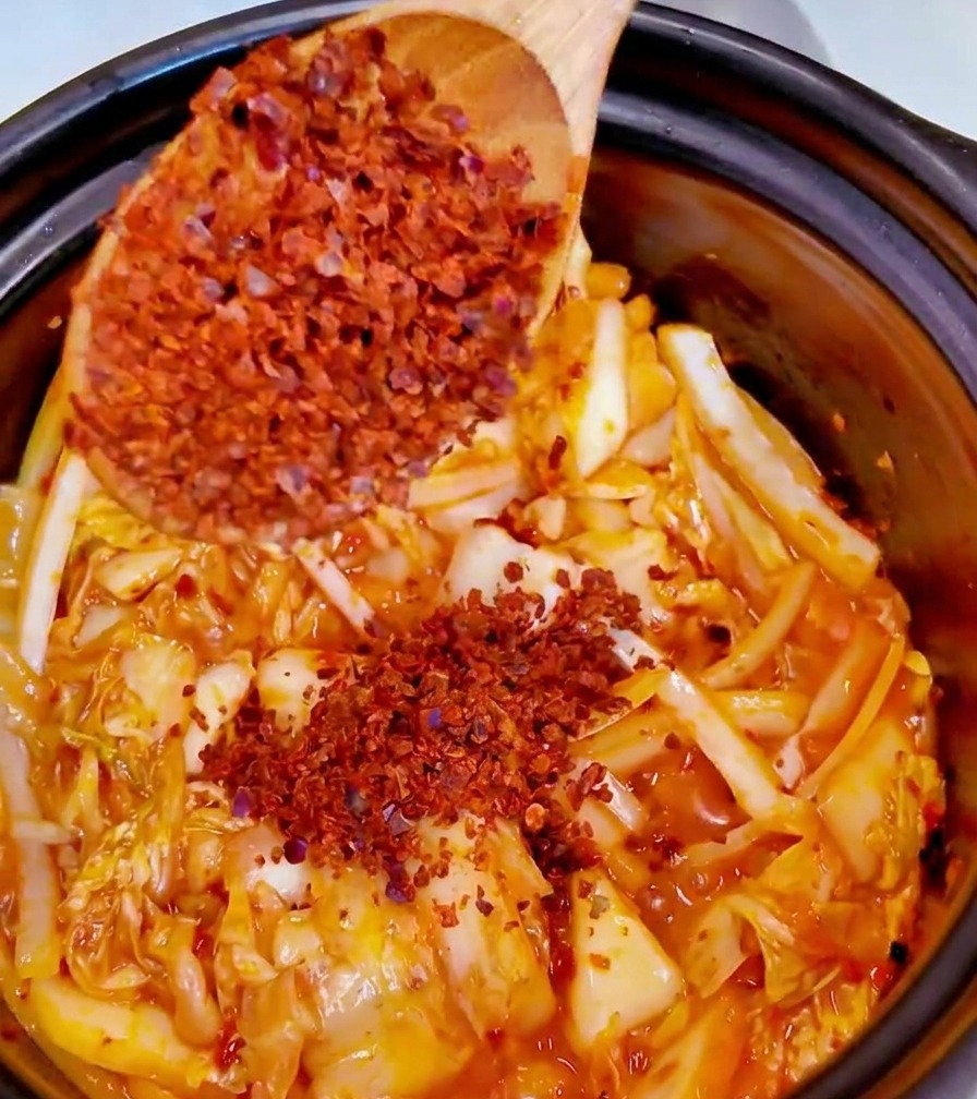 Ein Löffel mit feinem rotem Chilipulver wird in den Topf zu den restlichen Zutaten gegeben.